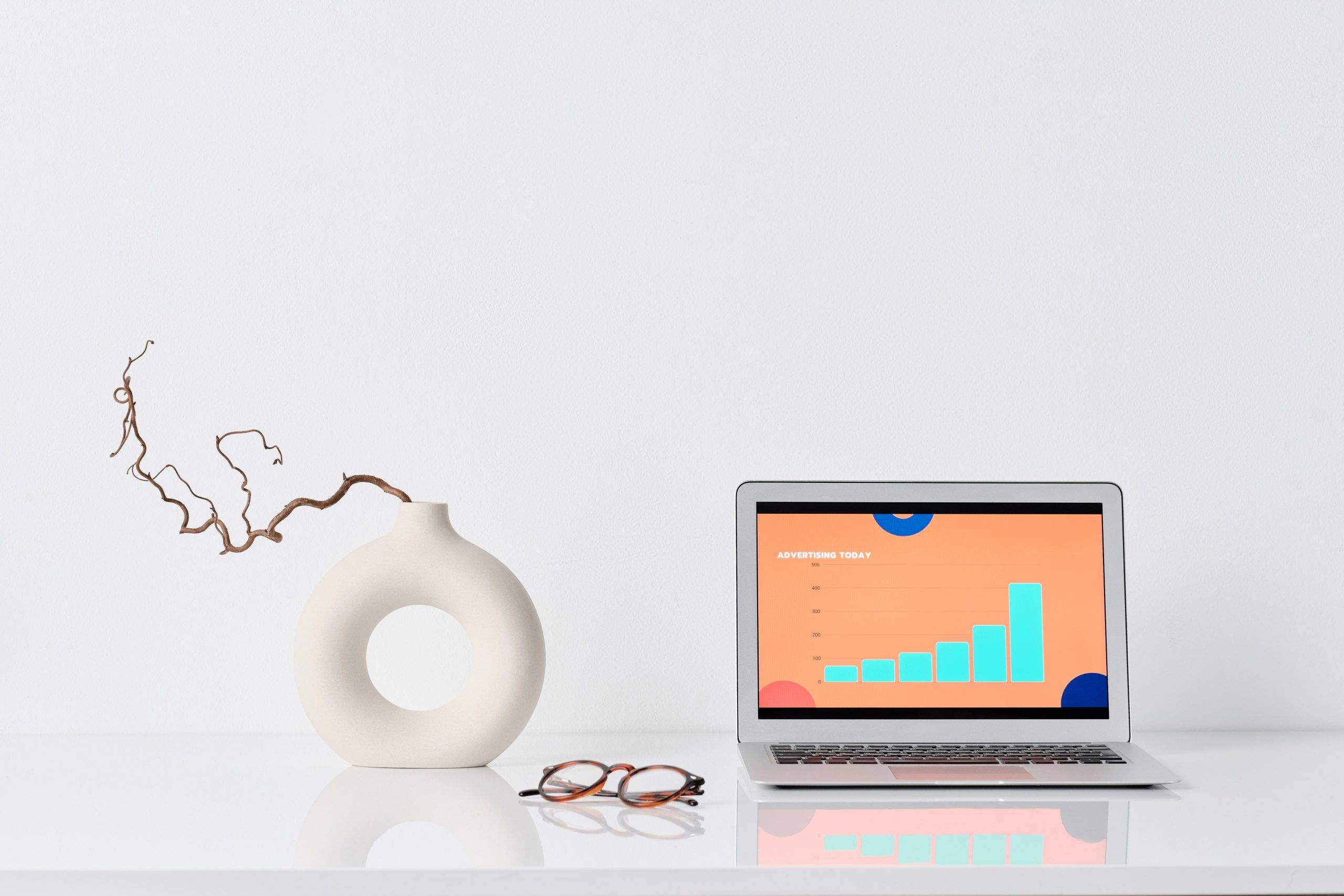 circular vase with a stem, glasses and a laptop on desk