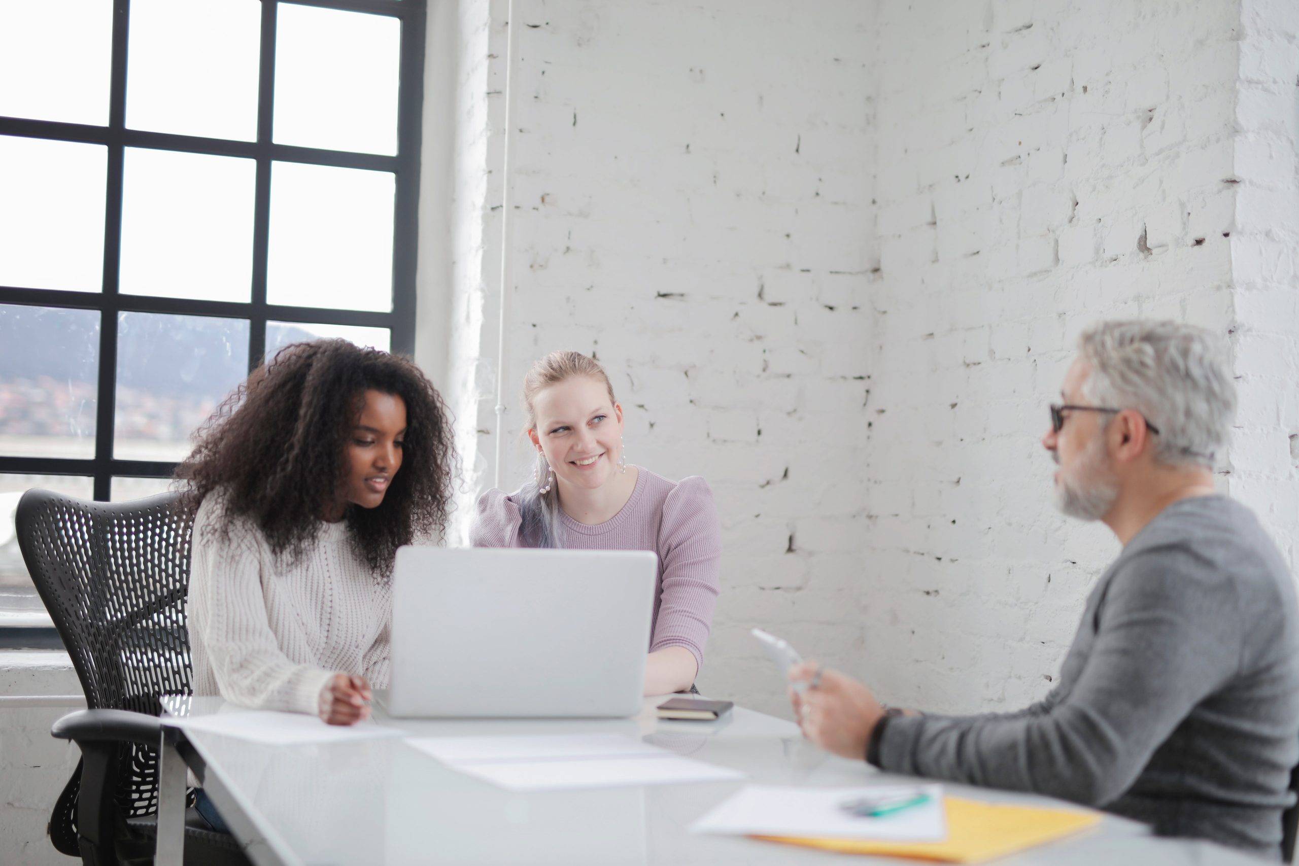 three people sitting at conference table. two ladies behind a computer and a man facing them.