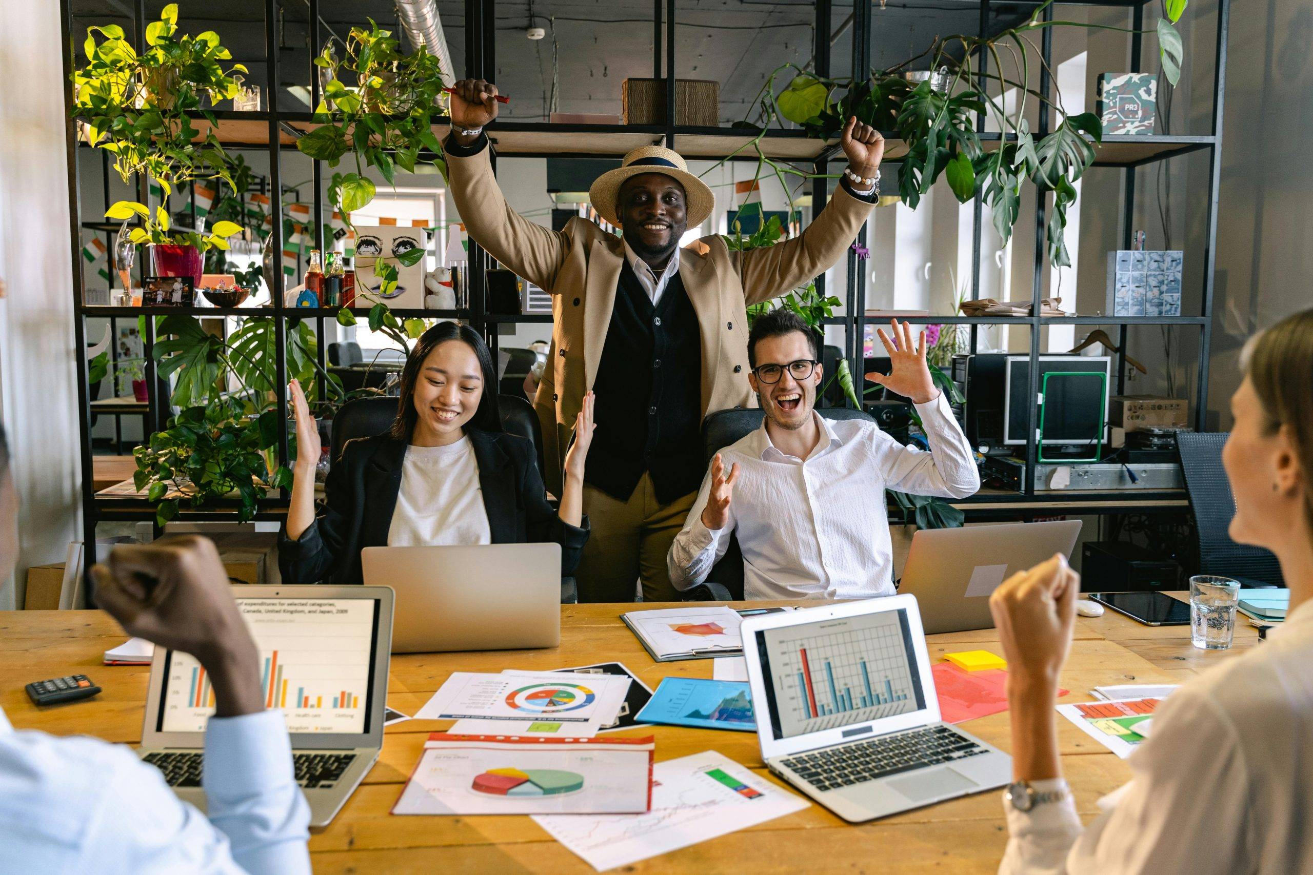 Business people celebrating around a desk with arms in the air. computers and data plans on the desk.