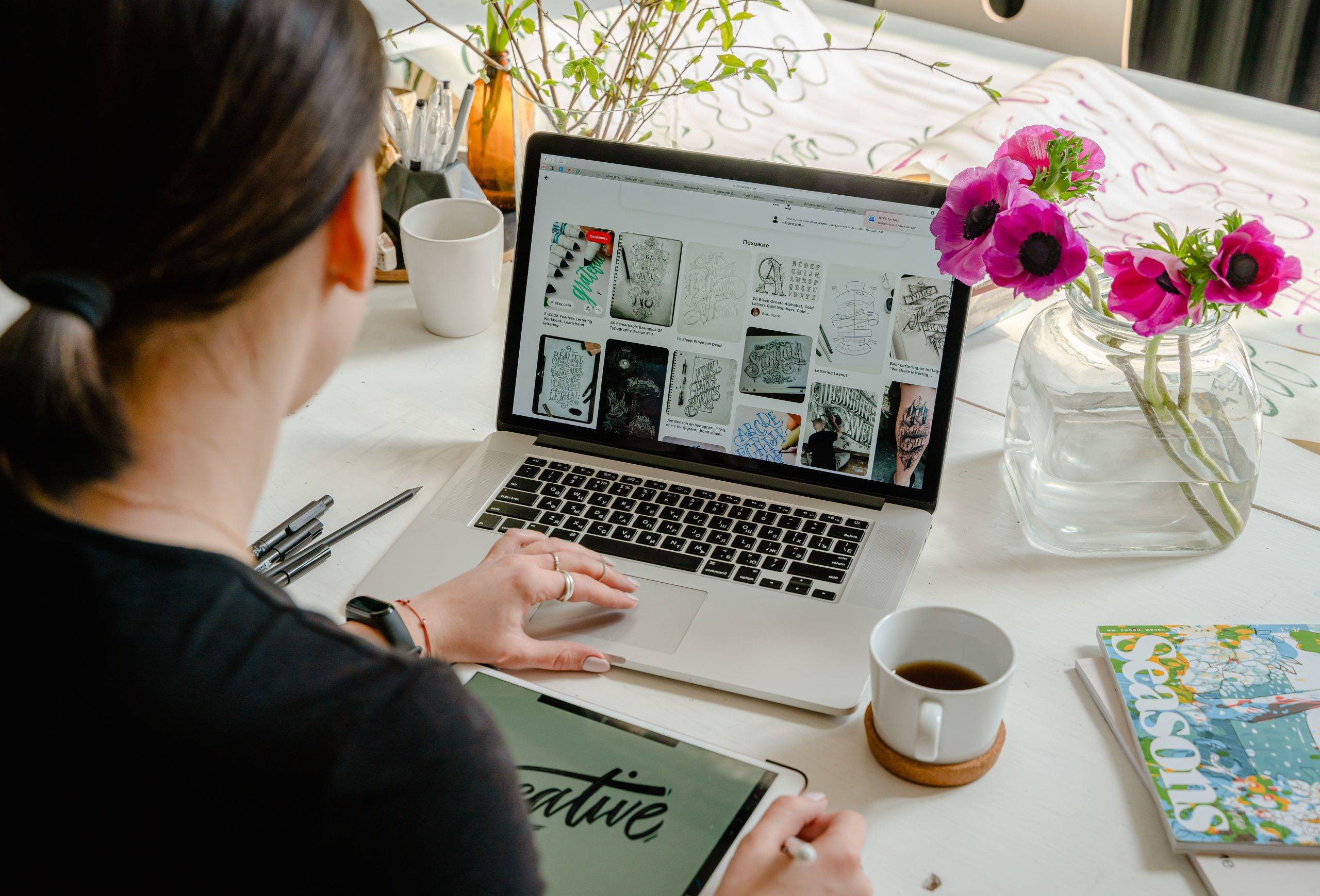 close up of the back of a female sitting at desk using the mouse pad on a laptop computer with a cup of coffee.