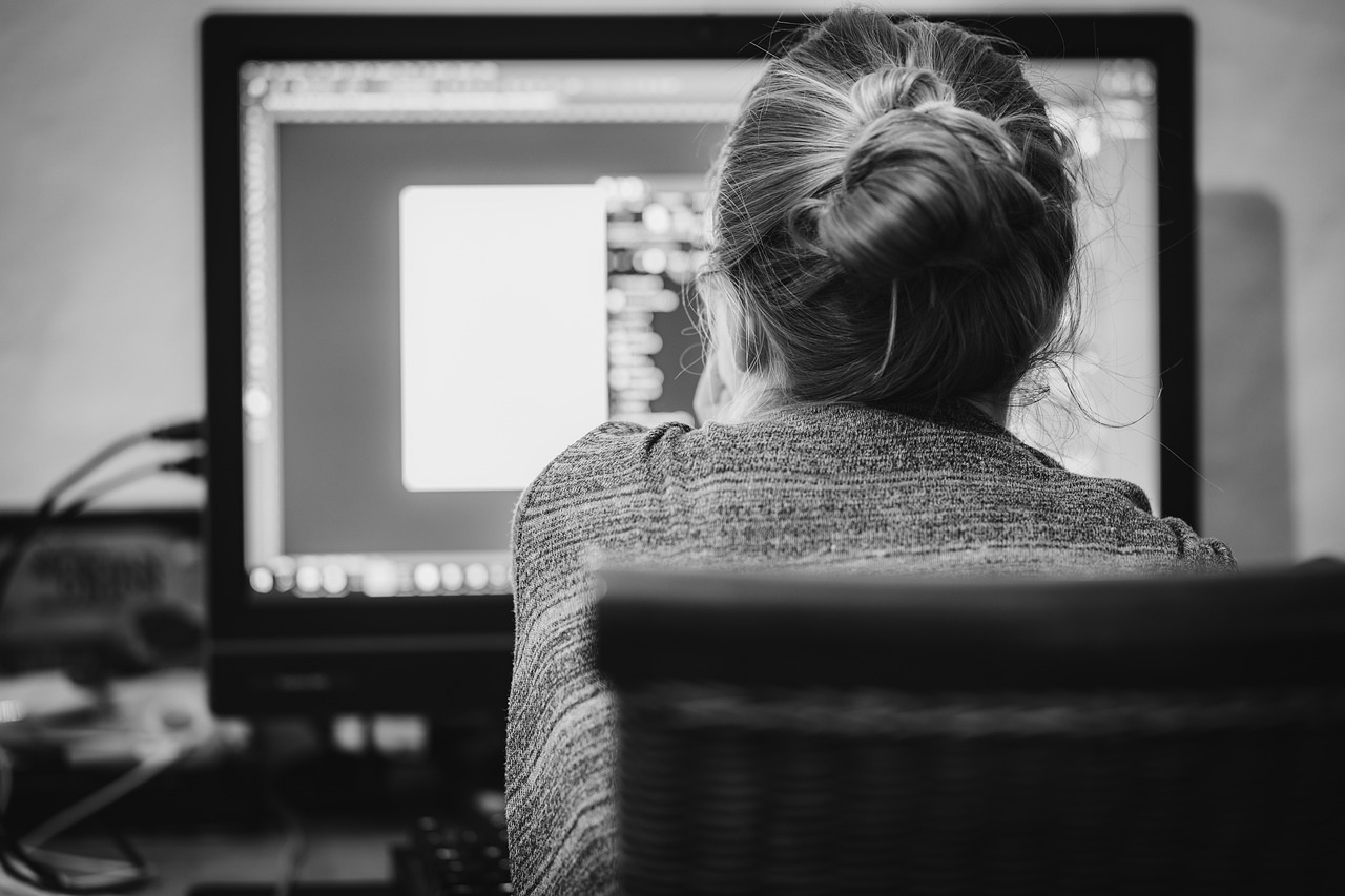 back of a woman sitting in chair at computer desk writing ad copy.