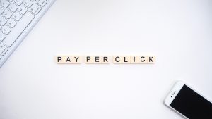 letter tiles spelling out "pay per click" on a desk with a cell phone.